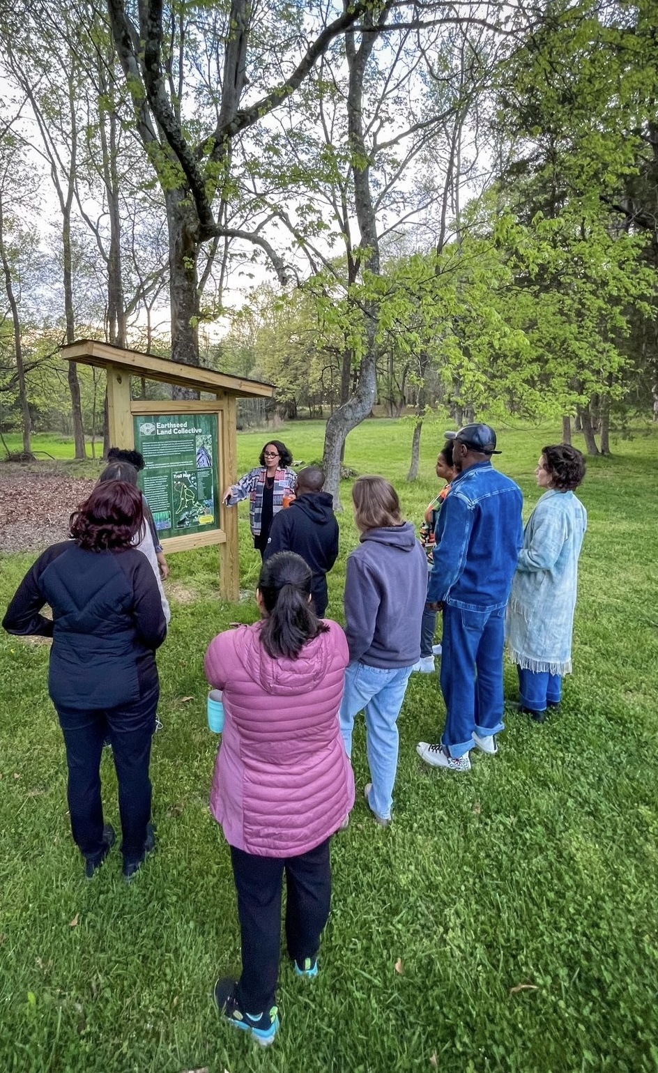 Image of a small group of people on the land being guided in front of the Trail Map Kiosk